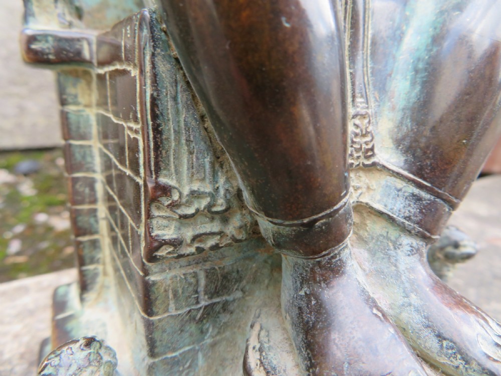 A dark copper alloy sculpture depicting Buddha seated on an ornate throne with legs lowered in the European posture. View XXX