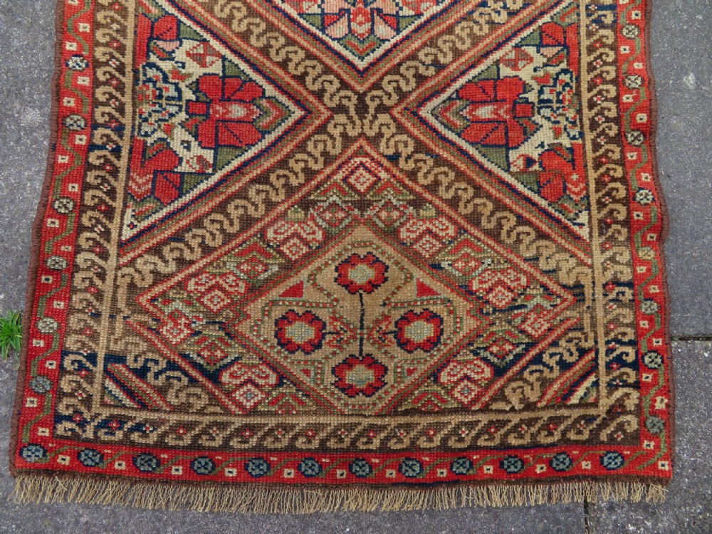 An antique North West Persian Kurdish hand-knotted wool narrow hallway runner featuring repeating diamond medallions in terracotta red, brown, and cream tones. View III