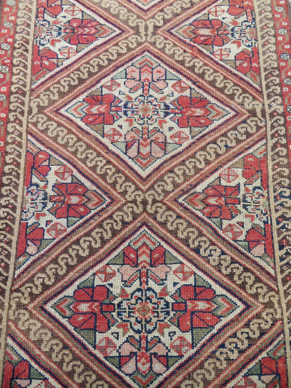 An antique North West Persian Kurdish hand-knotted wool narrow hallway runner featuring repeating diamond medallions in terracotta red, brown, and cream tones. View IV