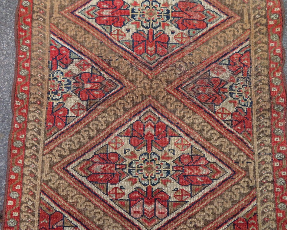 An antique North West Persian Kurdish hand-knotted wool narrow hallway runner featuring repeating diamond medallions in terracotta red, brown, and cream tones. View V