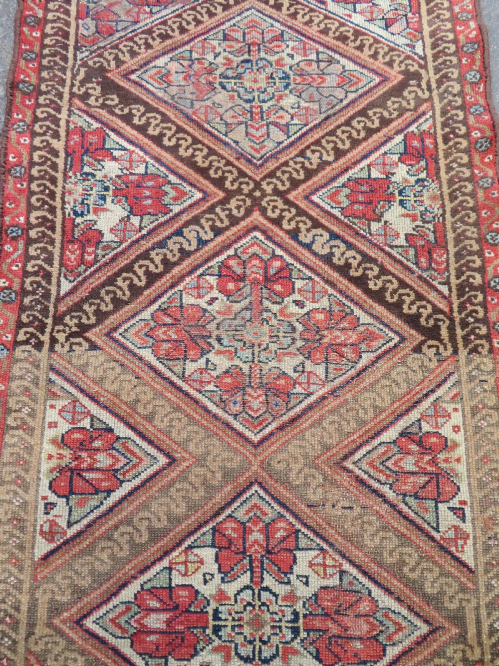 An antique North West Persian Kurdish hand-knotted wool narrow hallway runner featuring repeating diamond medallions in terracotta red, brown, and cream tones. View VI