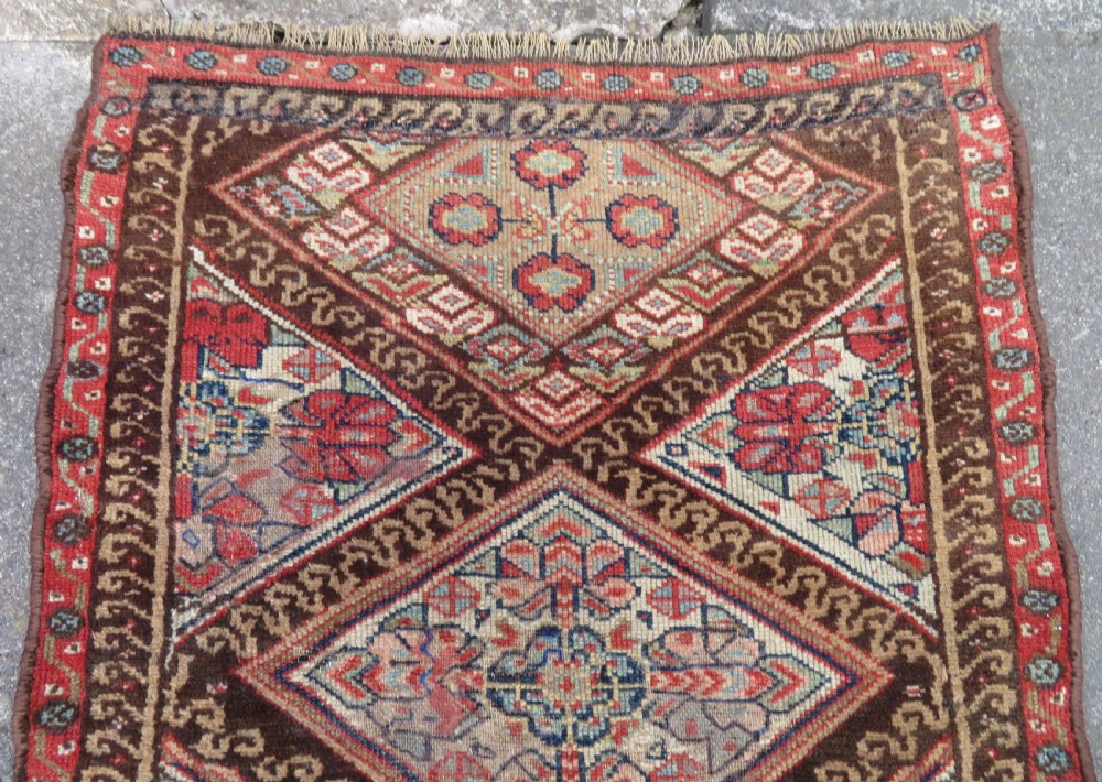 An antique North West Persian Kurdish hand-knotted wool narrow hallway runner featuring repeating diamond medallions in terracotta red, brown, and cream tones. View VII