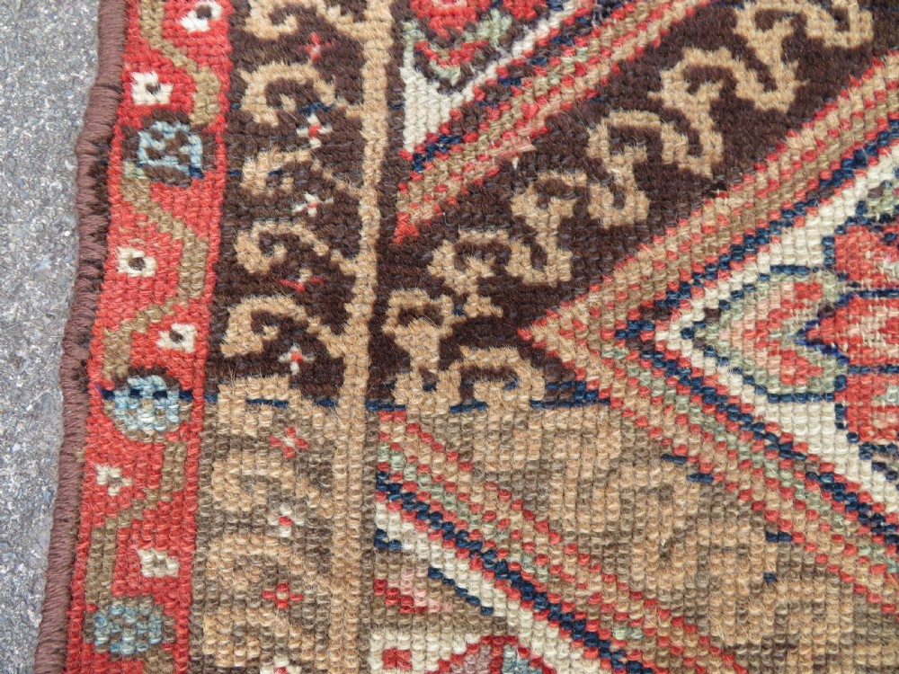 An antique North West Persian Kurdish hand-knotted wool narrow hallway runner featuring repeating diamond medallions in terracotta red, brown, and cream tones. View VIII