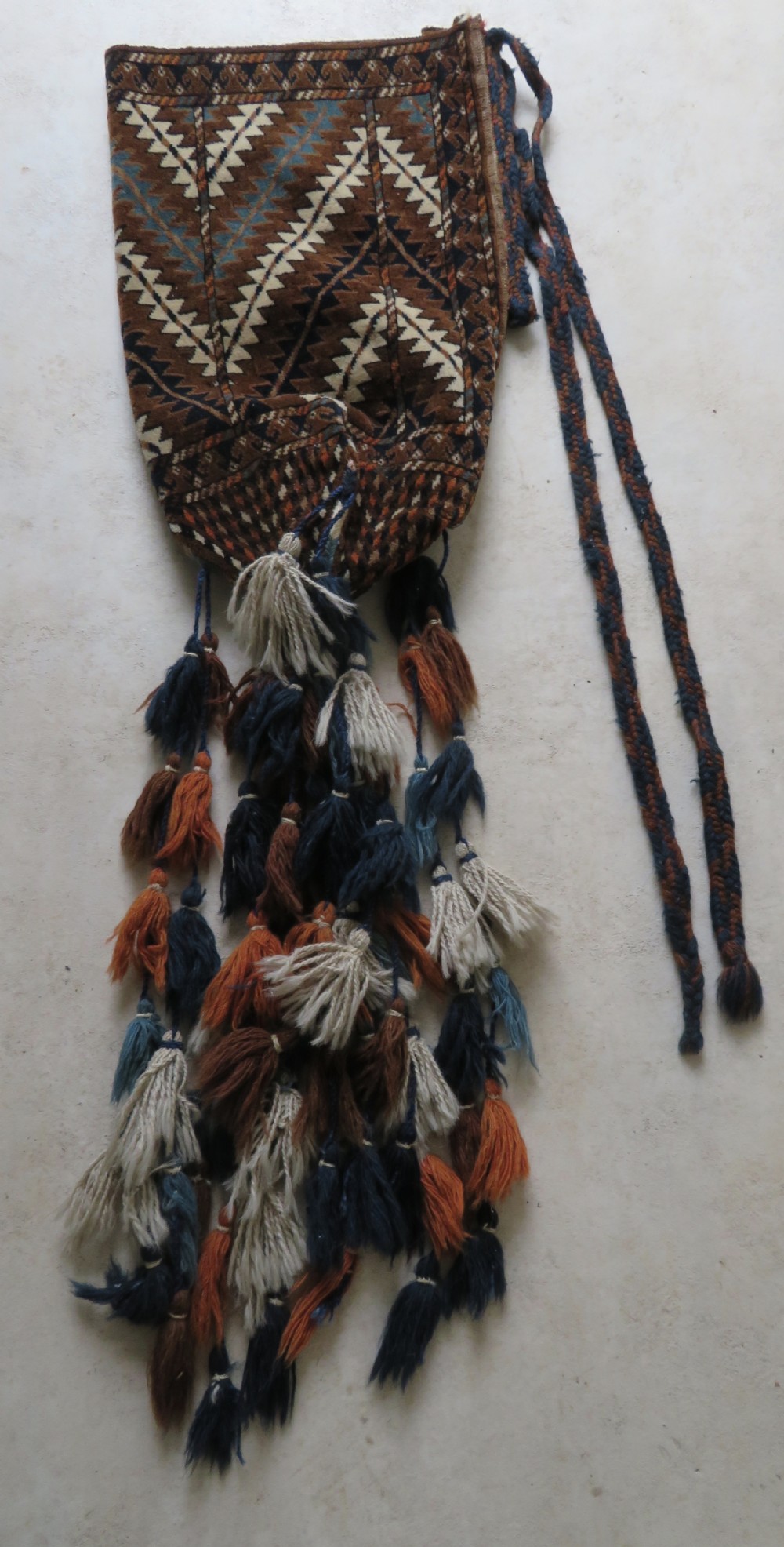 A hand-woven Yomut Turkmen Ok Bash tent-pole bag featuring geometric chevron patterns in rust brown, indigo, and cream wool, finished with braided ties and multi-coloured tassels. View II