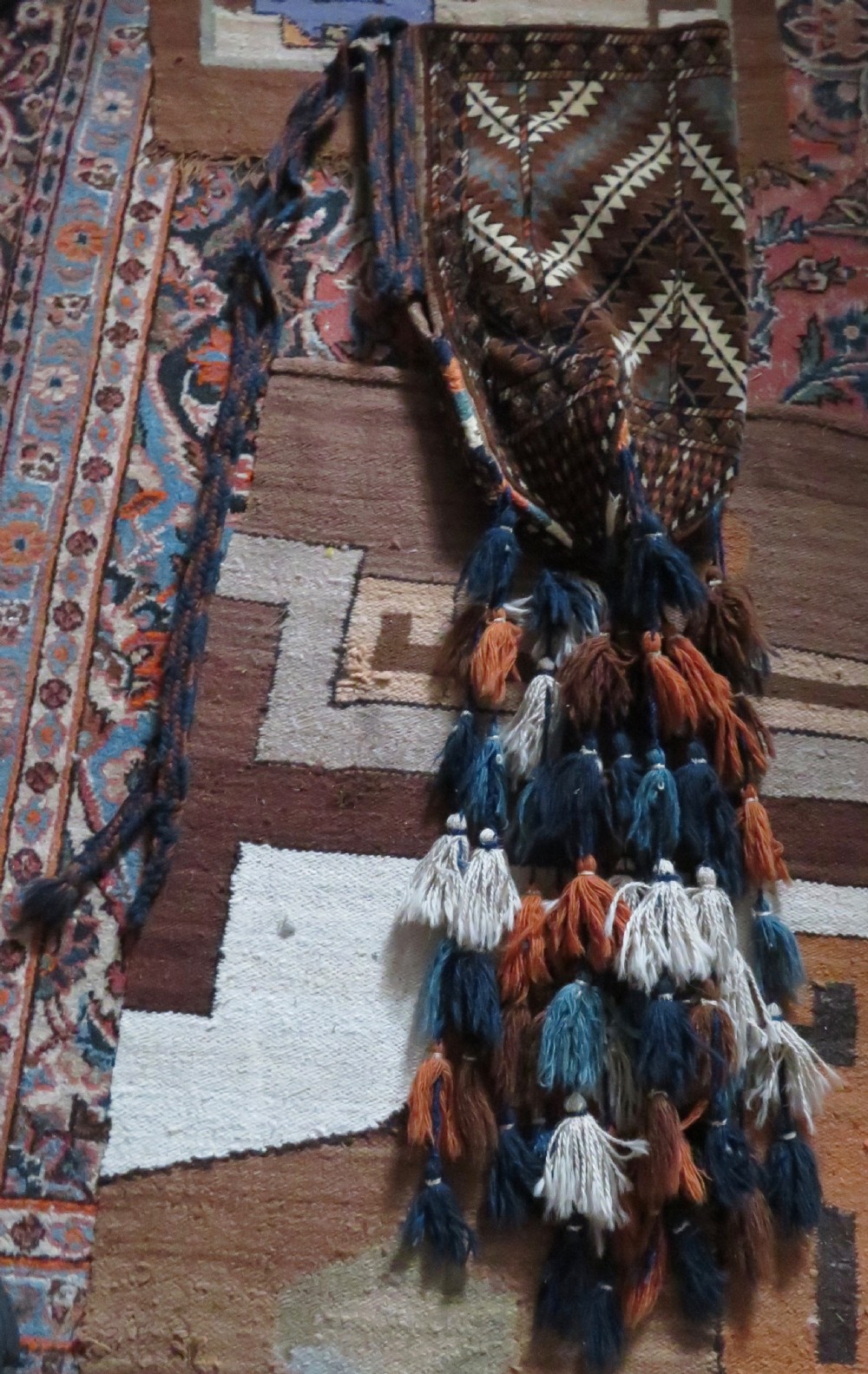 A hand-woven Yomut Turkmen Ok Bash tent-pole bag featuring geometric chevron patterns in rust brown, indigo, and cream wool, finished with braided ties and multi-coloured tassels. View III