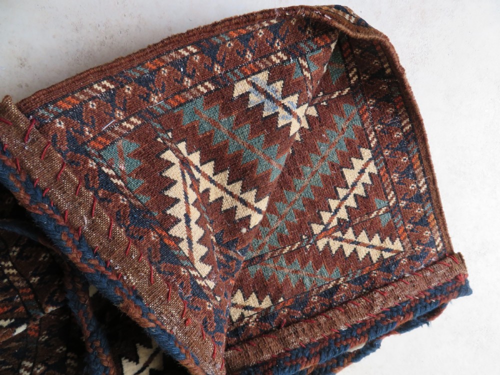 A hand-woven Yomut Turkmen Ok Bash tent-pole bag featuring geometric chevron patterns in rust brown, indigo, and cream wool, finished with braided ties and multi-coloured tassels. View VI