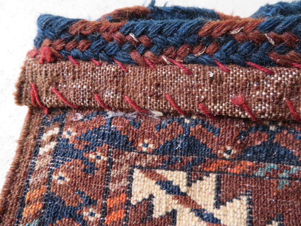 A hand-woven Yomut Turkmen Ok Bash tent-pole bag featuring geometric chevron patterns in rust brown, indigo, and cream wool, finished with braided ties and multi-coloured tassels. View VII