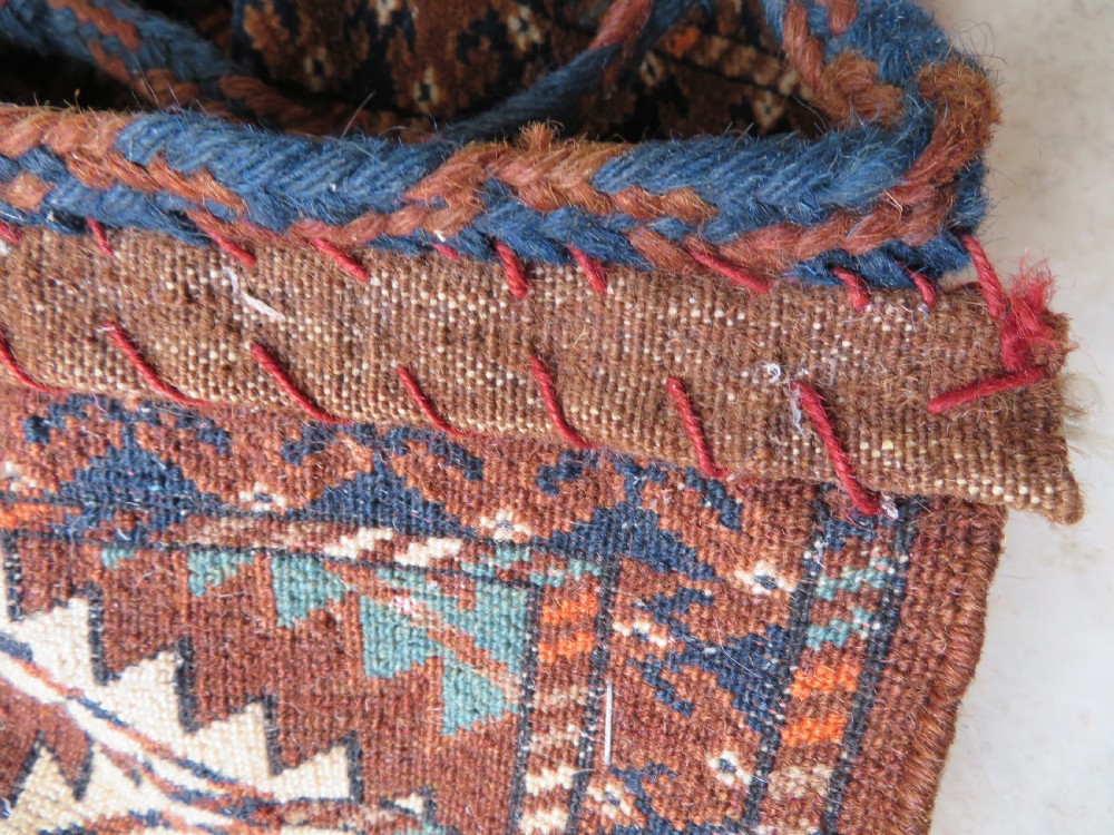 A hand-woven Yomut Turkmen Ok Bash tent-pole bag featuring geometric chevron patterns in rust brown, indigo, and cream wool, finished with braided ties and multi-coloured tassels. View VIII