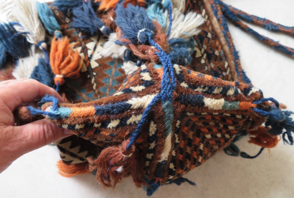 A hand-woven Yomut Turkmen Ok Bash tent-pole bag featuring geometric chevron patterns in rust brown, indigo, and cream wool, finished with braided ties and multi-coloured tassels. View IX