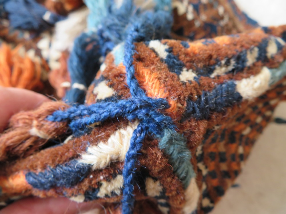 A hand-woven Yomut Turkmen Ok Bash tent-pole bag featuring geometric chevron patterns in rust brown, indigo, and cream wool, finished with braided ties and multi-coloured tassels. View X