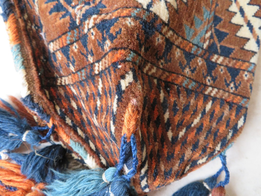 A hand-woven Yomut Turkmen Ok Bash tent-pole bag featuring geometric chevron patterns in rust brown, indigo, and cream wool, finished with braided ties and multi-coloured tassels. View XX