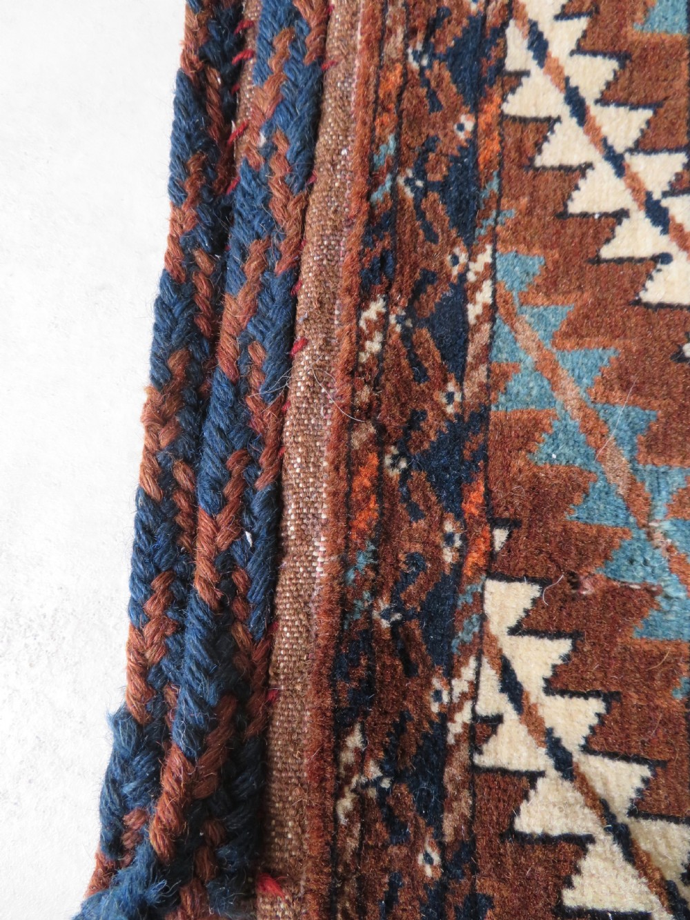 A hand-woven Yomut Turkmen Ok Bash tent-pole bag featuring geometric chevron patterns in rust brown, indigo, and cream wool, finished with braided ties and multi-coloured tassels. View XXI
