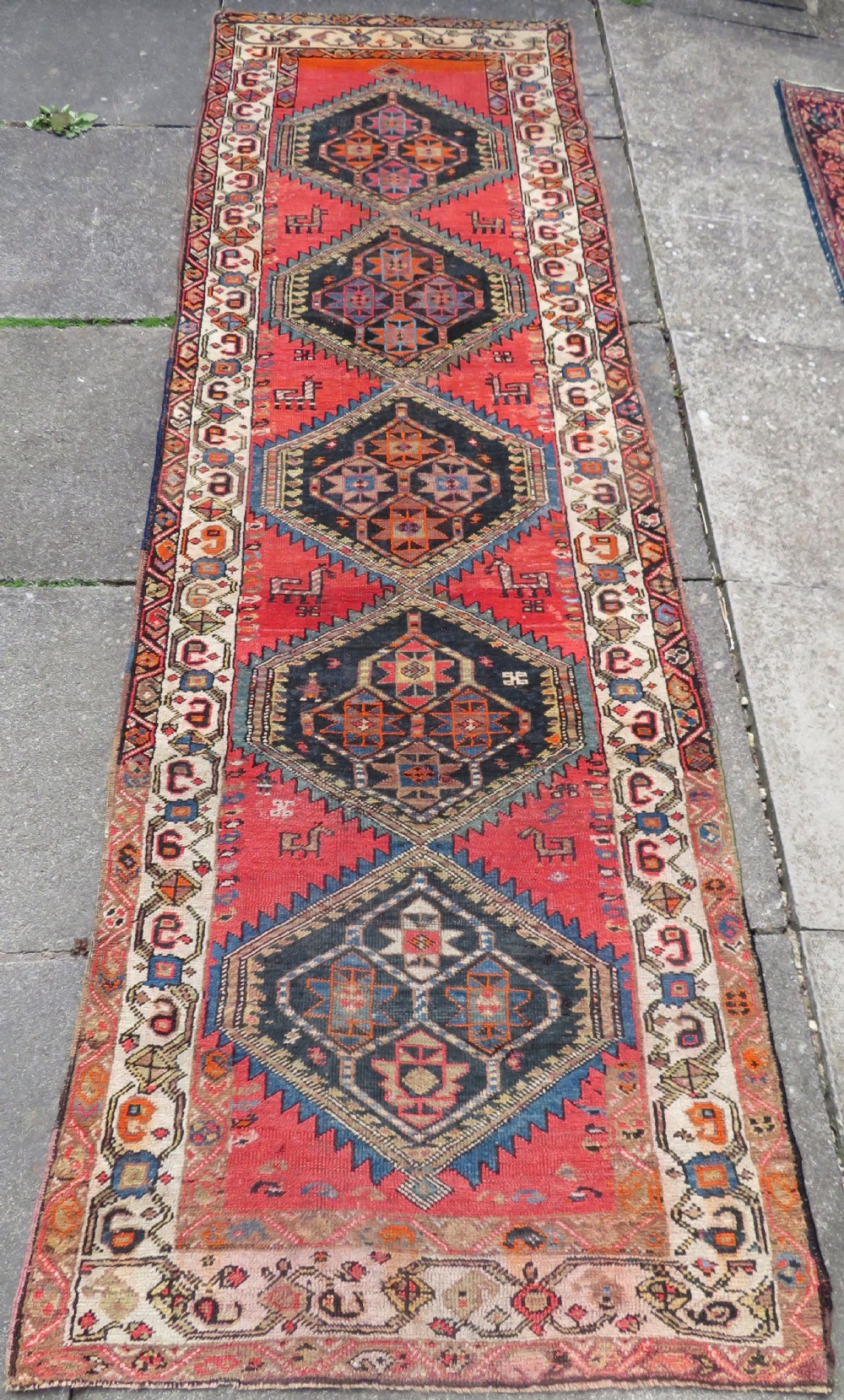 A hand-knotted antique Persian Kurdish wool runner rug with five central diamond medallions on a red field framed by a patterned ivory border.