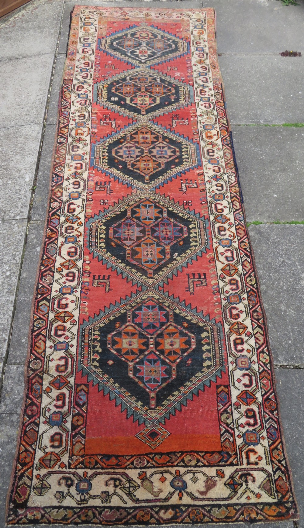 A hand-knotted antique Persian Kurdish wool runner rug with five central diamond medallions on a red field framed by a patterned ivory border. View II