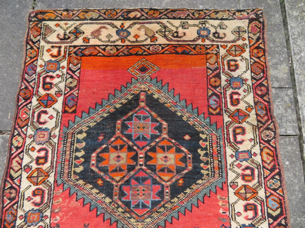 A hand-knotted antique Persian Kurdish wool runner rug with five central diamond medallions on a red field framed by a patterned ivory border. View III