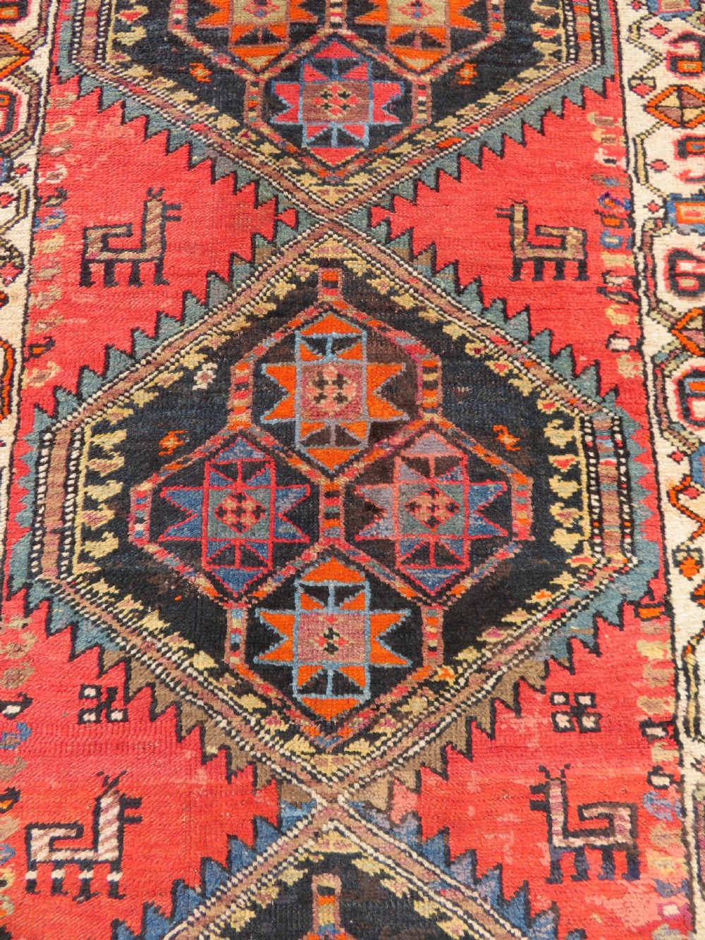A hand-knotted antique Persian Kurdish wool runner rug with five central diamond medallions on a red field framed by a patterned ivory border. View IV