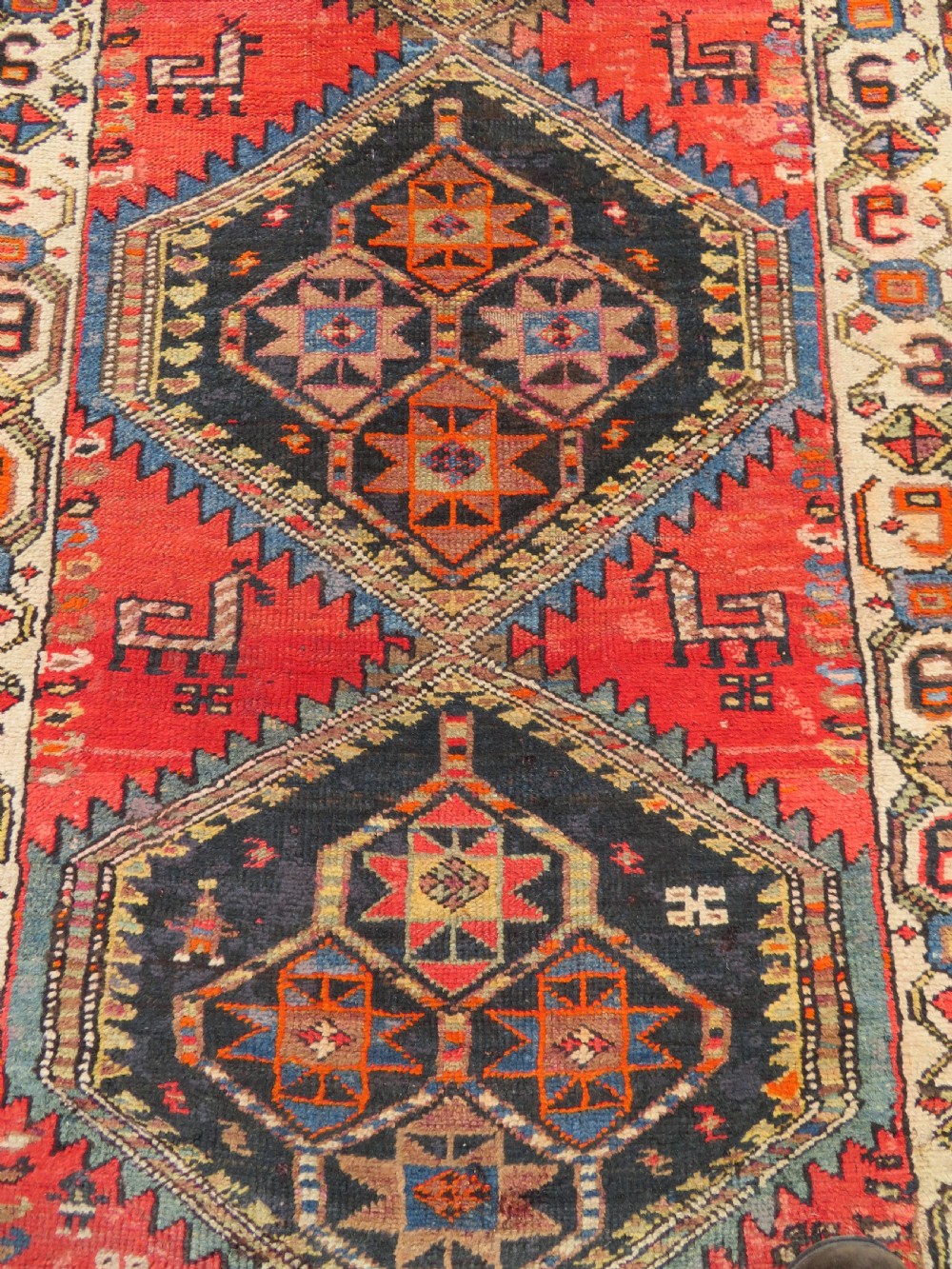 A hand-knotted antique Persian Kurdish wool runner rug with five central diamond medallions on a red field framed by a patterned ivory border. View V