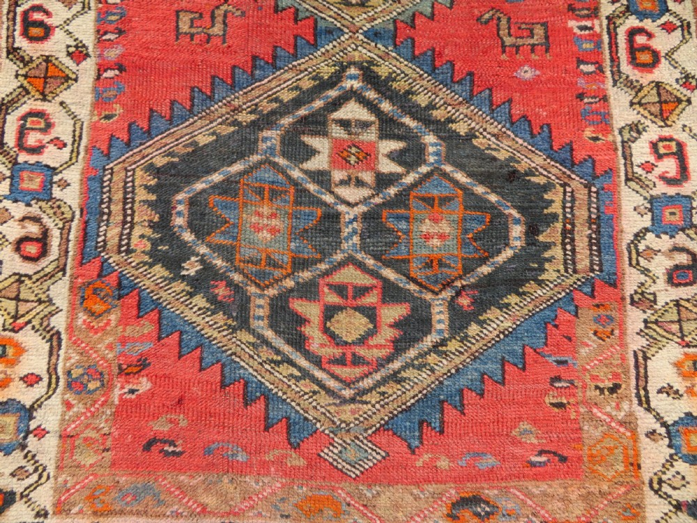 A hand-knotted antique Persian Kurdish wool runner rug with five central diamond medallions on a red field framed by a patterned ivory border. View VI