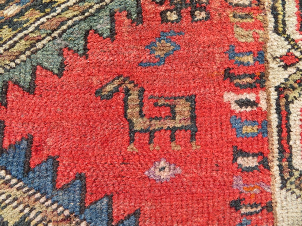 A hand-knotted antique Persian Kurdish wool runner rug with five central diamond medallions on a red field framed by a patterned ivory border. View VII