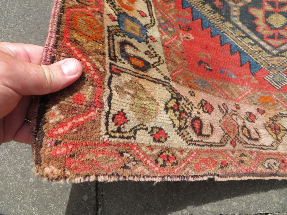 A hand-knotted antique Persian Kurdish wool runner rug with five central diamond medallions on a red field framed by a patterned ivory border. View XV