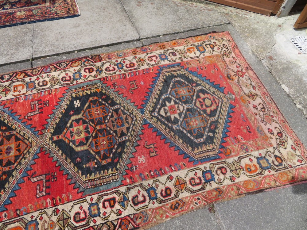 A hand-knotted antique Persian Kurdish wool runner rug with five central diamond medallions on a red field framed by a patterned ivory border. View XIX