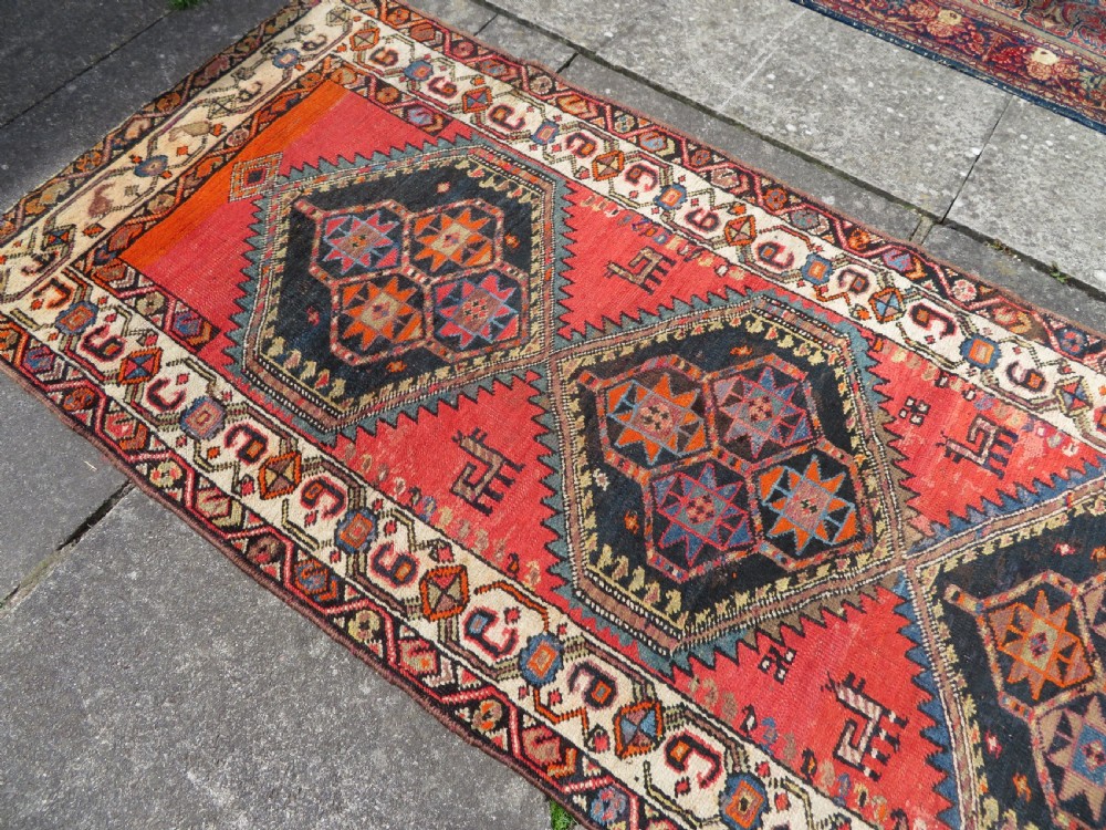 A hand-knotted antique Persian Kurdish wool runner rug with five central diamond medallions on a red field framed by a patterned ivory border. View XX