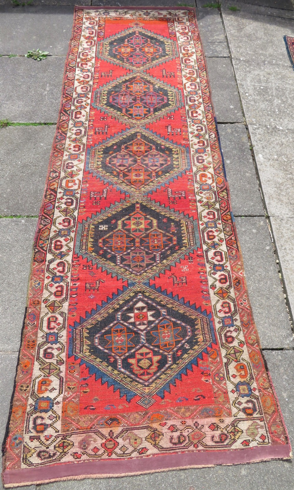 A hand-knotted antique Persian Kurdish wool runner rug with five central diamond medallions on a red field framed by a patterned ivory border. View XXI