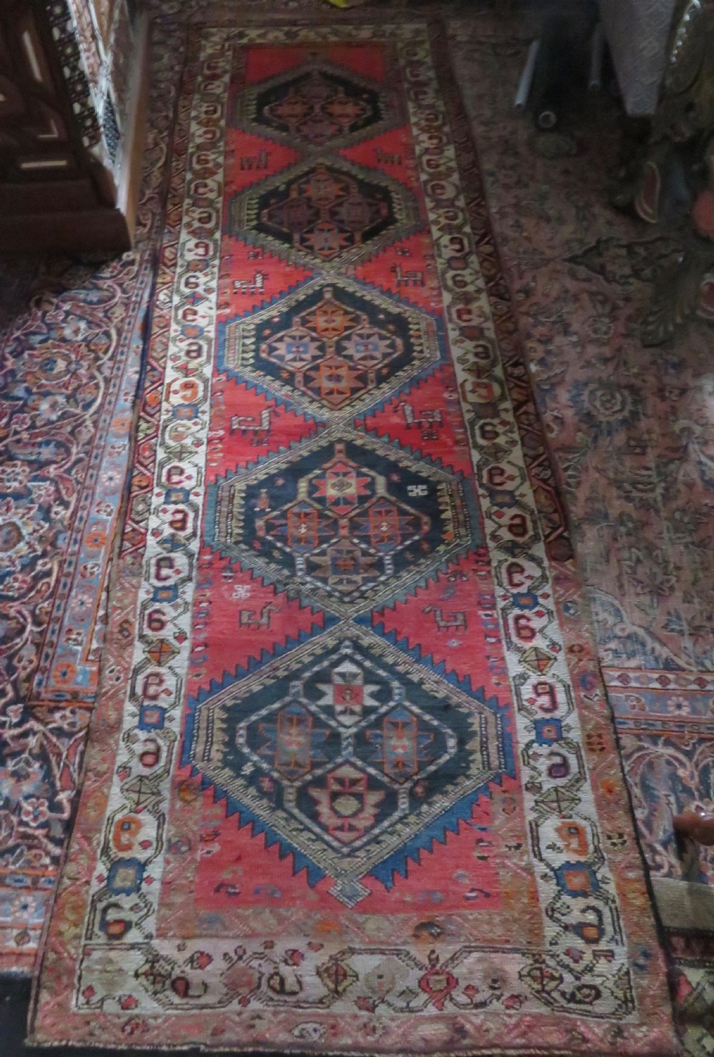 A hand-knotted antique Persian Kurdish wool runner rug with five central diamond medallions on a red field framed by a patterned ivory border. View XXV