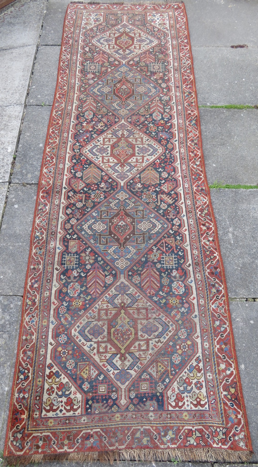An antique hand-knotted Qashqai wool runner rug featuring repeating geometric diamond medallions in red, blue, and cream tones. View II