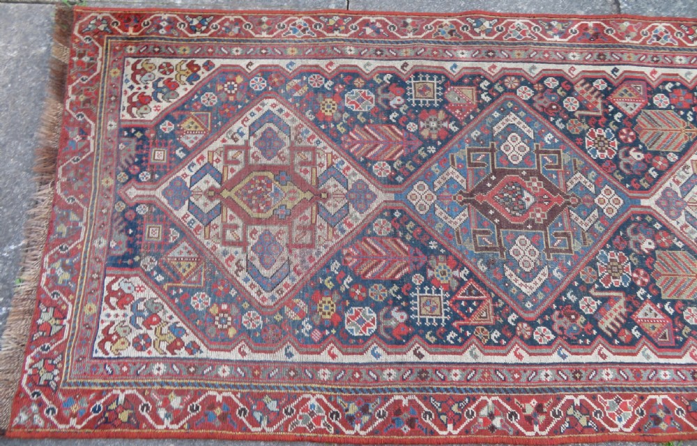 An antique hand-knotted Qashqai wool runner rug featuring repeating geometric diamond medallions in red, blue, and cream tones. View III