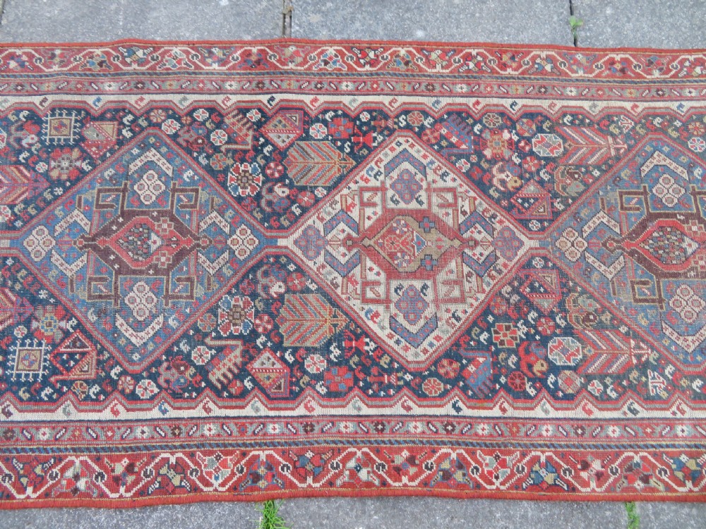 An antique hand-knotted Qashqai wool runner rug featuring repeating geometric diamond medallions in red, blue, and cream tones. View IV