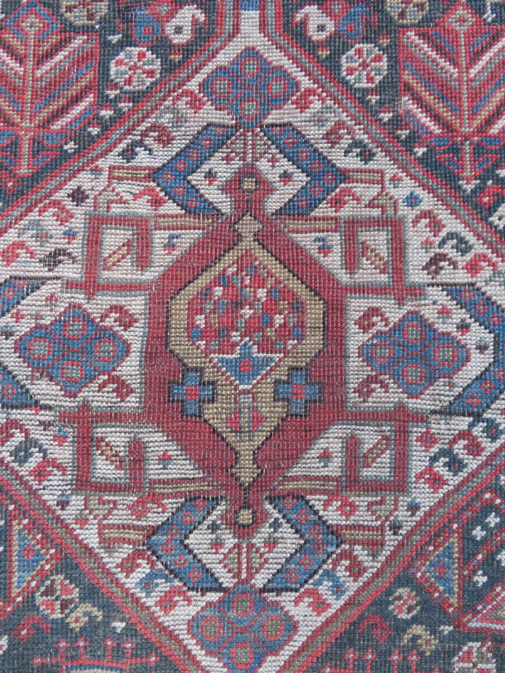 An antique hand-knotted Qashqai wool runner rug featuring repeating geometric diamond medallions in red, blue, and cream tones. View VII