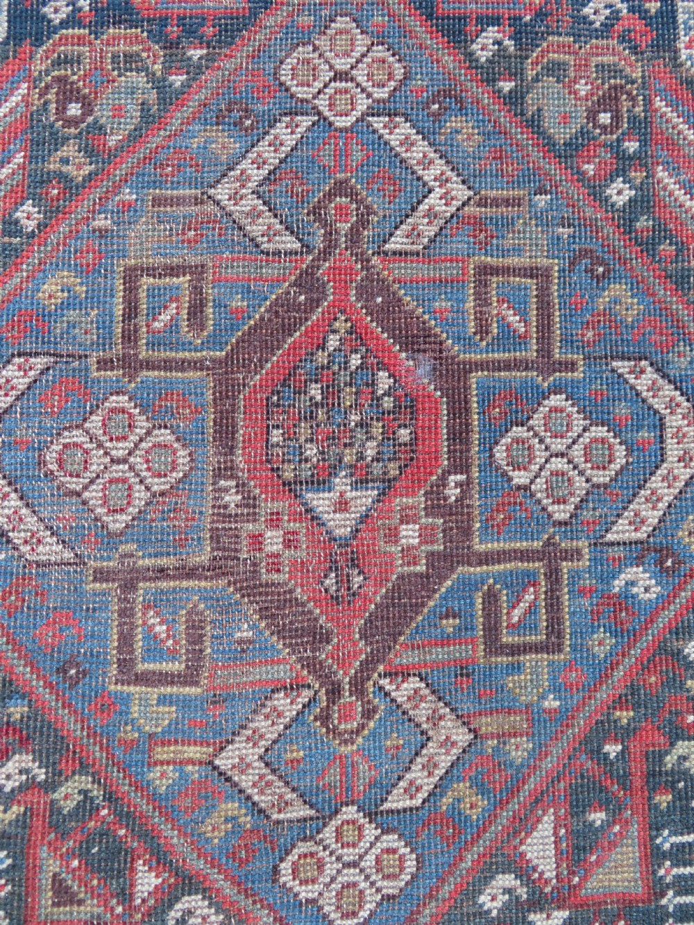 An antique hand-knotted Qashqai wool runner rug featuring repeating geometric diamond medallions in red, blue, and cream tones. View VIII