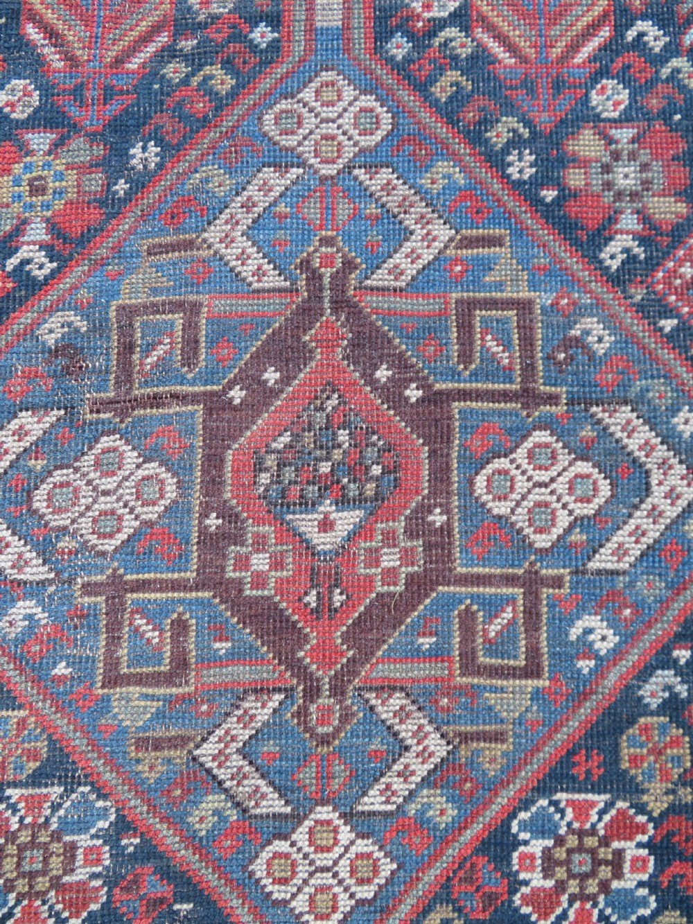 An antique hand-knotted Qashqai wool runner rug featuring repeating geometric diamond medallions in red, blue, and cream tones. View X