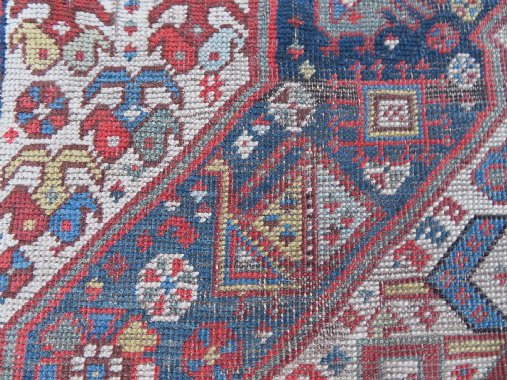 An antique hand-knotted Qashqai wool runner rug featuring repeating geometric diamond medallions in red, blue, and cream tones. View XII