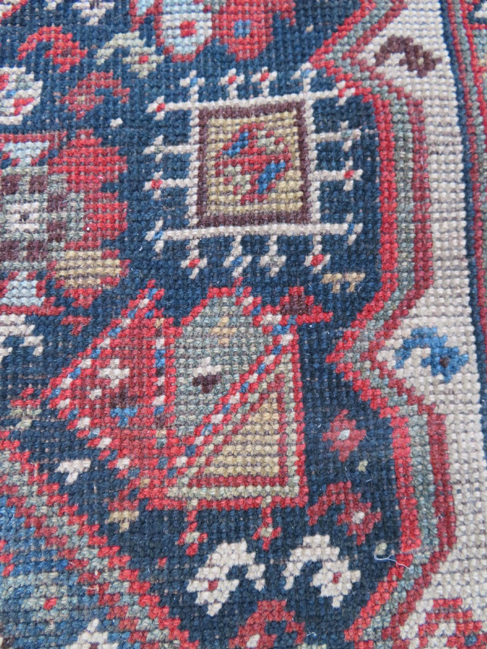An antique hand-knotted Qashqai wool runner rug featuring repeating geometric diamond medallions in red, blue, and cream tones. View XIV