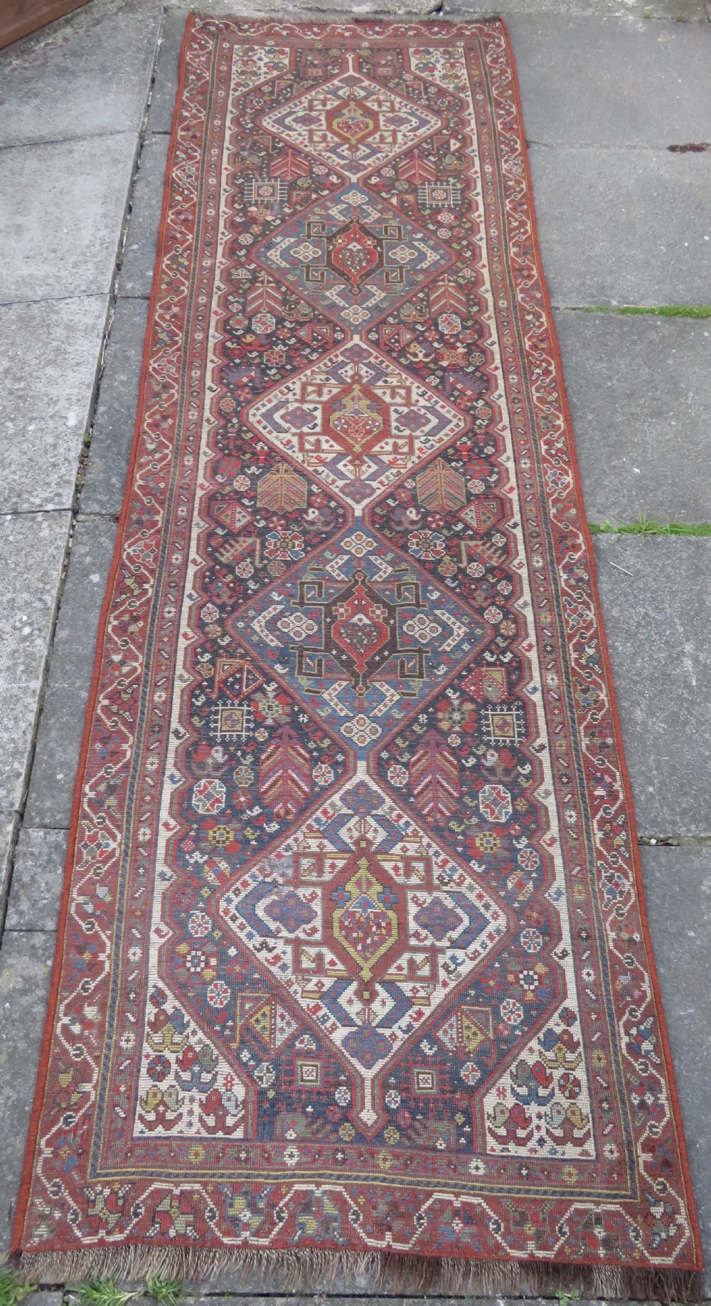 An antique hand-knotted Qashqai wool runner rug featuring repeating geometric diamond medallions in red, blue, and cream tones. View XXV