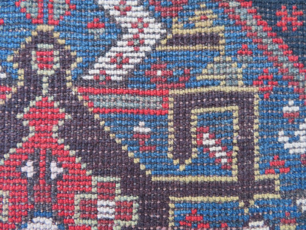 An antique hand-knotted Qashqai wool runner rug featuring repeating geometric diamond medallions in red, blue, and cream tones. View XXVI