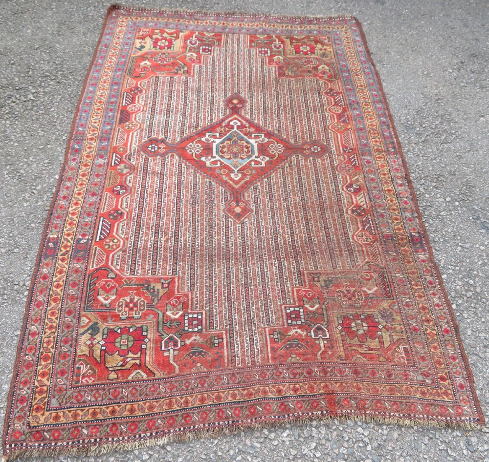 An antique hand-knotted South Persian Khamseh rug featuring a central diamond medallion surrounded by a striped field and geometric borders in shades of terracotta red, navy blue, and cream. View II