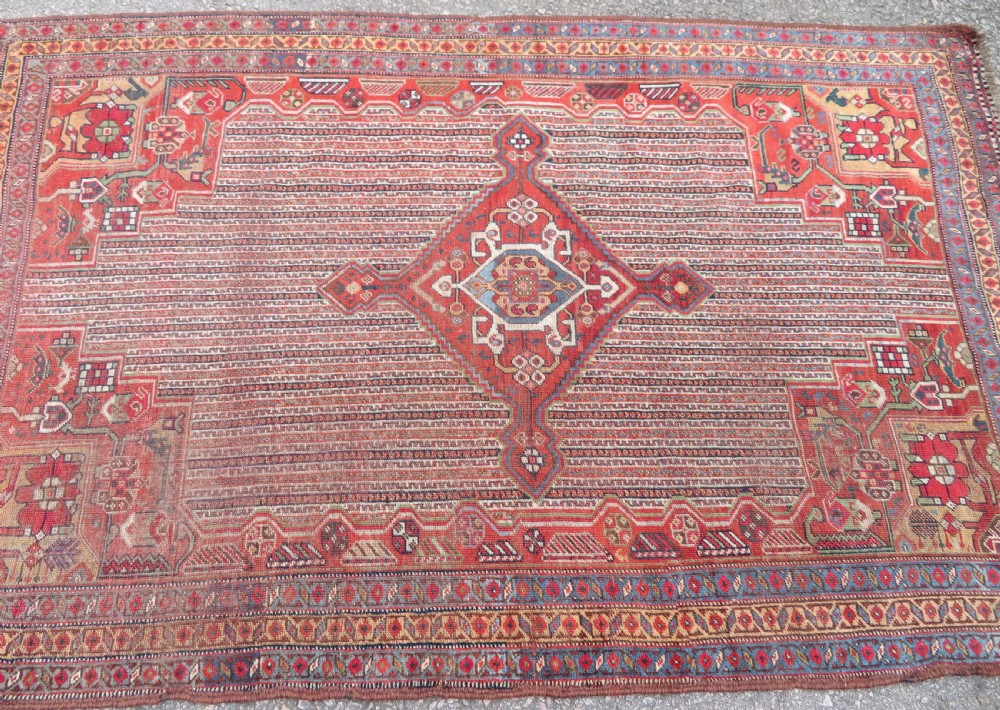 An antique hand-knotted South Persian Khamseh rug featuring a central diamond medallion surrounded by a striped field and geometric borders in shades of terracotta red, navy blue, and cream. View III