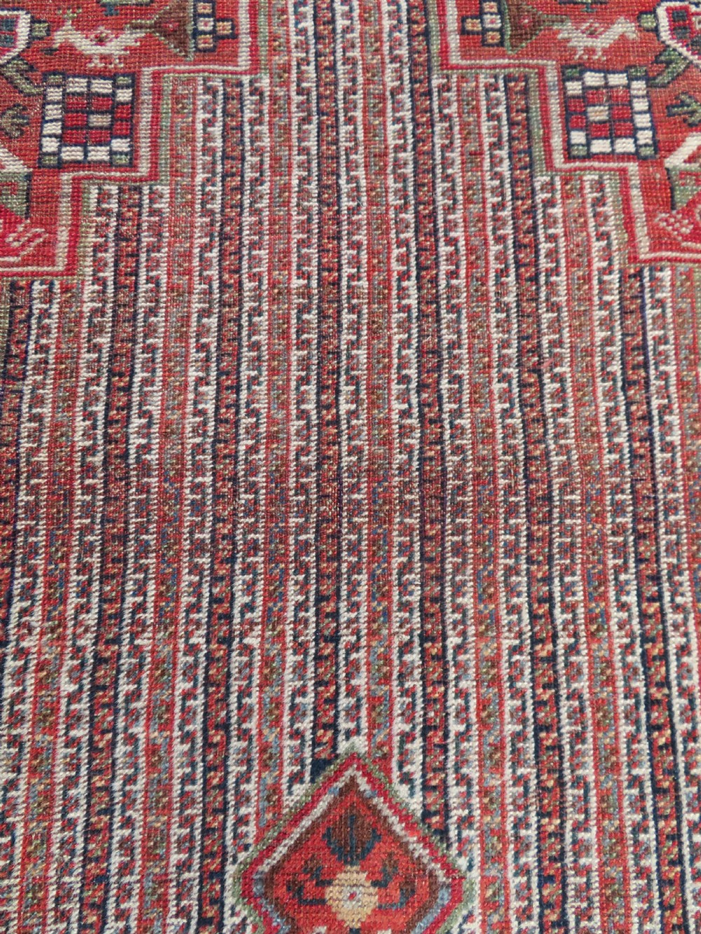 An antique hand-knotted South Persian Khamseh rug featuring a central diamond medallion surrounded by a striped field and geometric borders in shades of terracotta red, navy blue, and cream. View IX