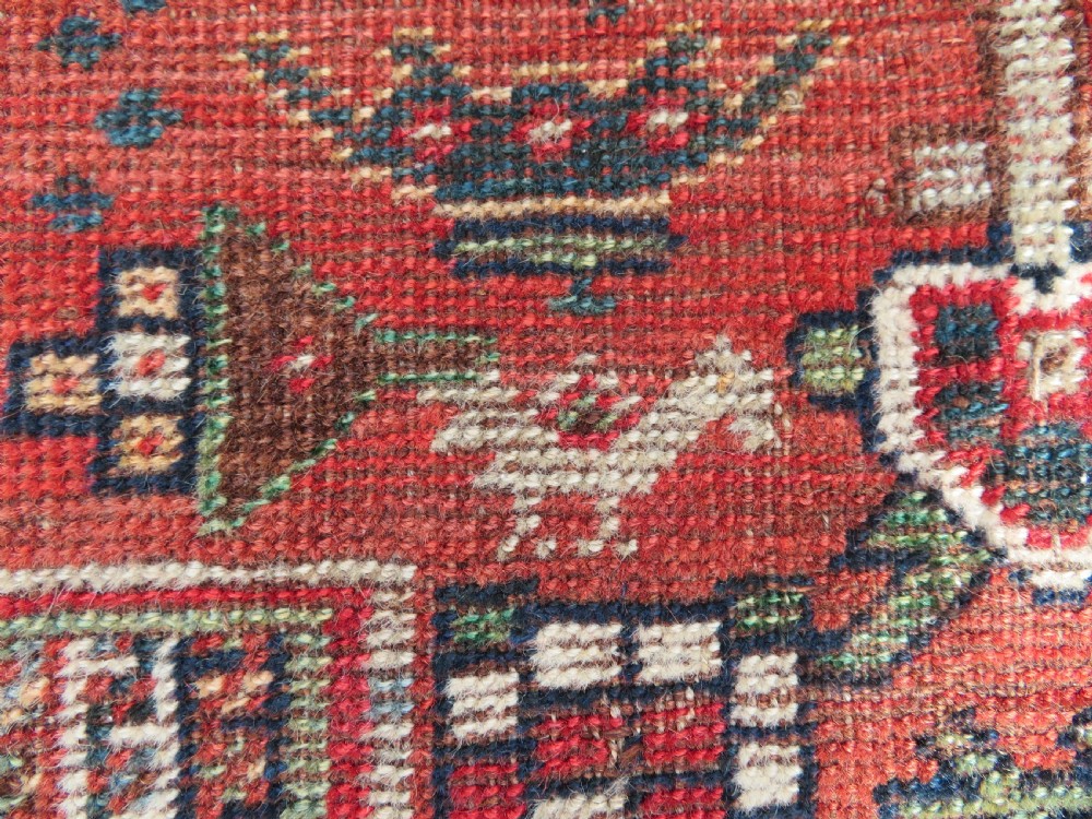 An antique hand-knotted South Persian Khamseh rug featuring a central diamond medallion surrounded by a striped field and geometric borders in shades of terracotta red, navy blue, and cream. View X