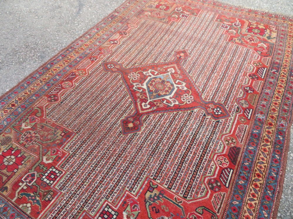 An antique hand-knotted South Persian Khamseh rug featuring a central diamond medallion surrounded by a striped field and geometric borders in shades of terracotta red, navy blue, and cream. View XV