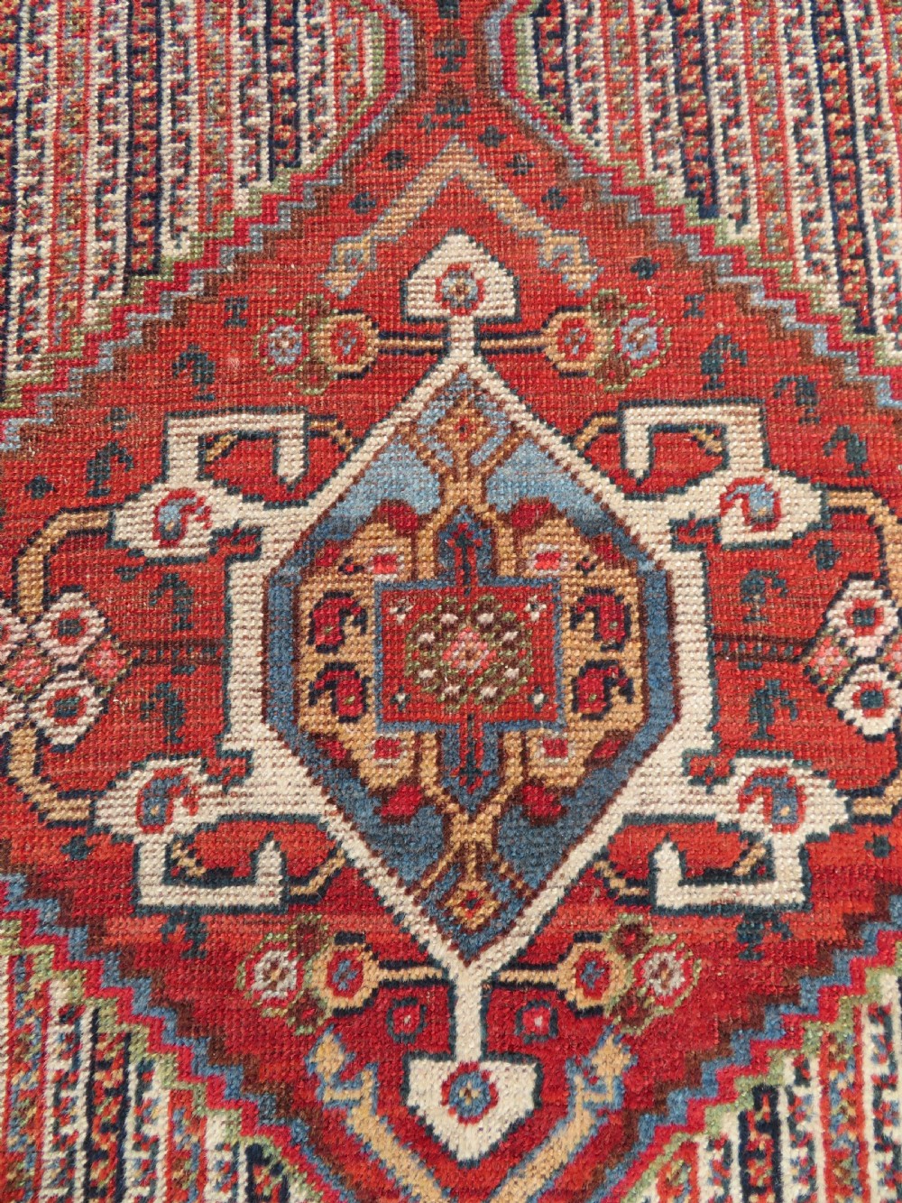 An antique hand-knotted South Persian Khamseh rug featuring a central diamond medallion surrounded by a striped field and geometric borders in shades of terracotta red, navy blue, and cream. View XVII