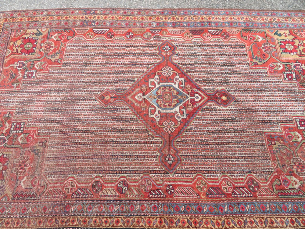 An antique hand-knotted South Persian Khamseh rug featuring a central diamond medallion surrounded by a striped field and geometric borders in shades of terracotta red, navy blue, and cream. View XIX