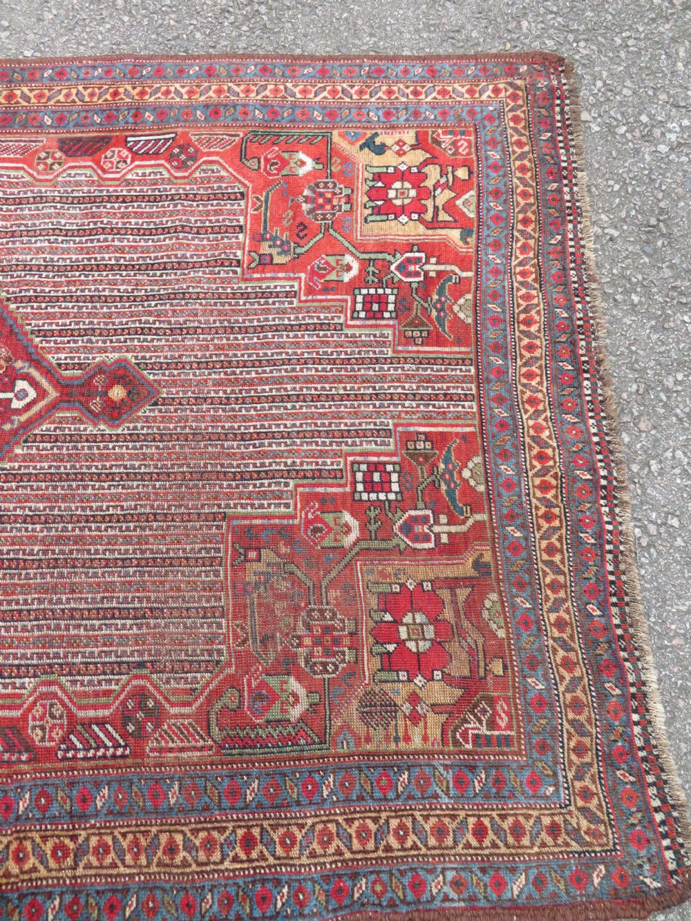 An antique hand-knotted South Persian Khamseh rug featuring a central diamond medallion surrounded by a striped field and geometric borders in shades of terracotta red, navy blue, and cream. View XXI