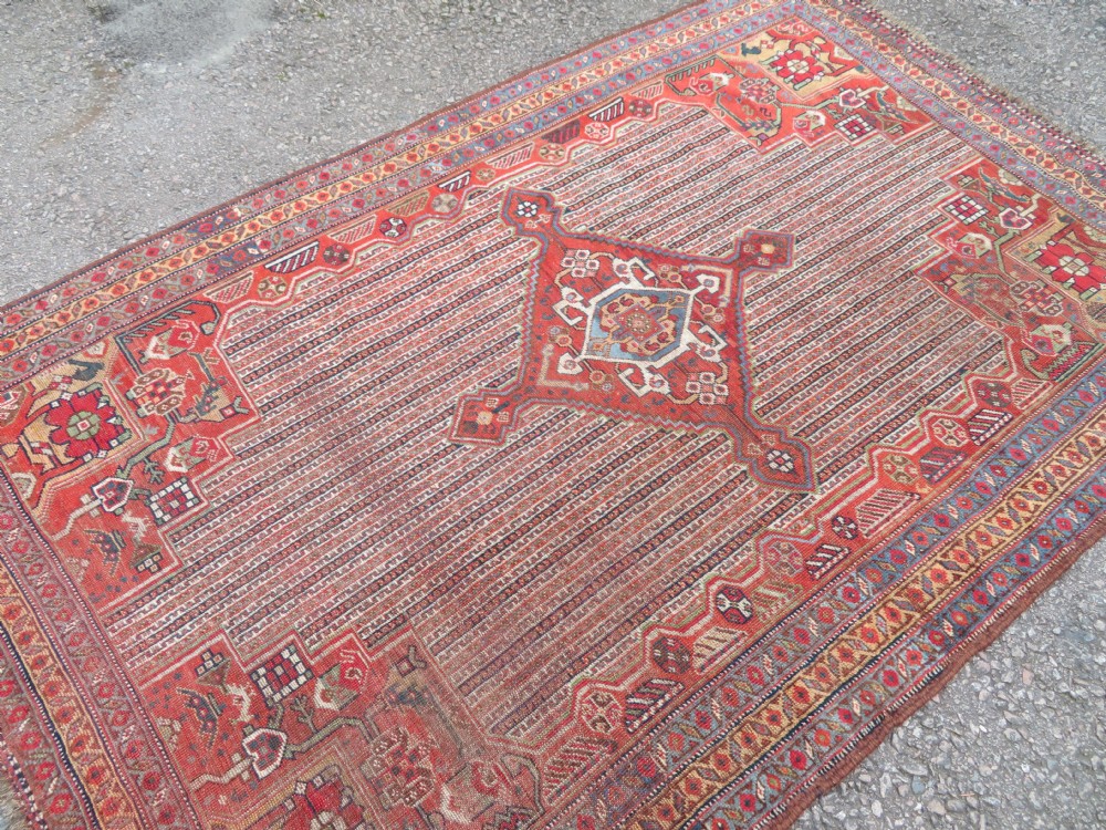 An antique hand-knotted South Persian Khamseh rug featuring a central diamond medallion surrounded by a striped field and geometric borders in shades of terracotta red, navy blue, and cream. View XXIII