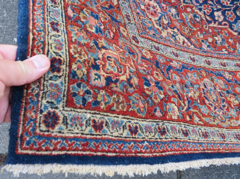 An antique hand-knotted Persian Kashan wool rug featuring a central ivory and red medallion surrounded by dense floral motifs on a dark blue field. View VIII