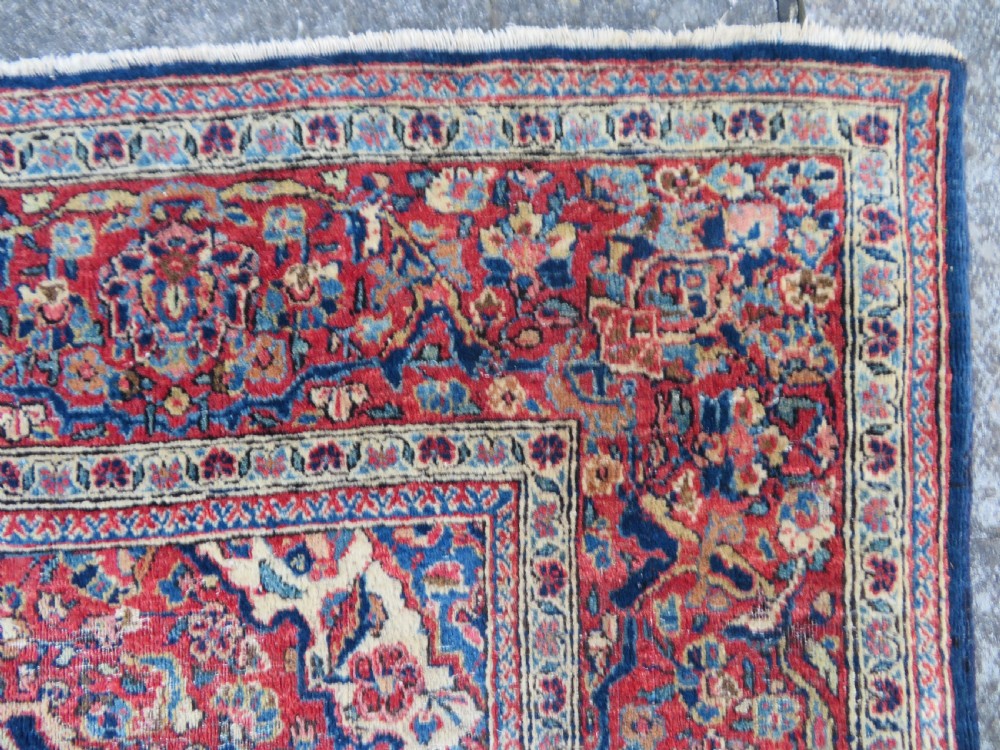 An antique hand-knotted Persian Kashan wool rug featuring a central ivory and red medallion surrounded by dense floral motifs on a dark blue field. View XI