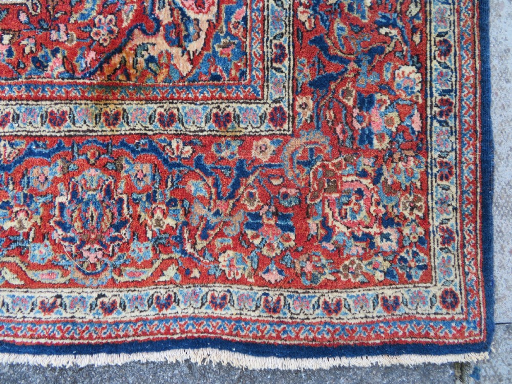 An antique hand-knotted Persian Kashan wool rug featuring a central ivory and red medallion surrounded by dense floral motifs on a dark blue field. View XII